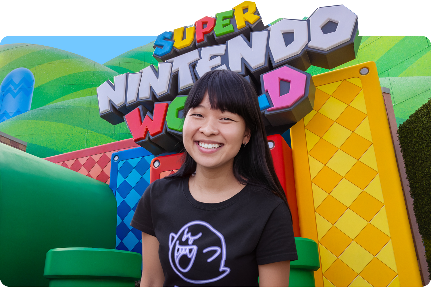 Person wearing a black t-shirt with a logo in front of a colorful 'Super Nintendo World' sign - click to shop SUPER NINTENDO WORLD™ castle with colorful architecture and a character in the foreground - click to see more details about SUPER NINTENDO WORLD™ Adult Merch now!