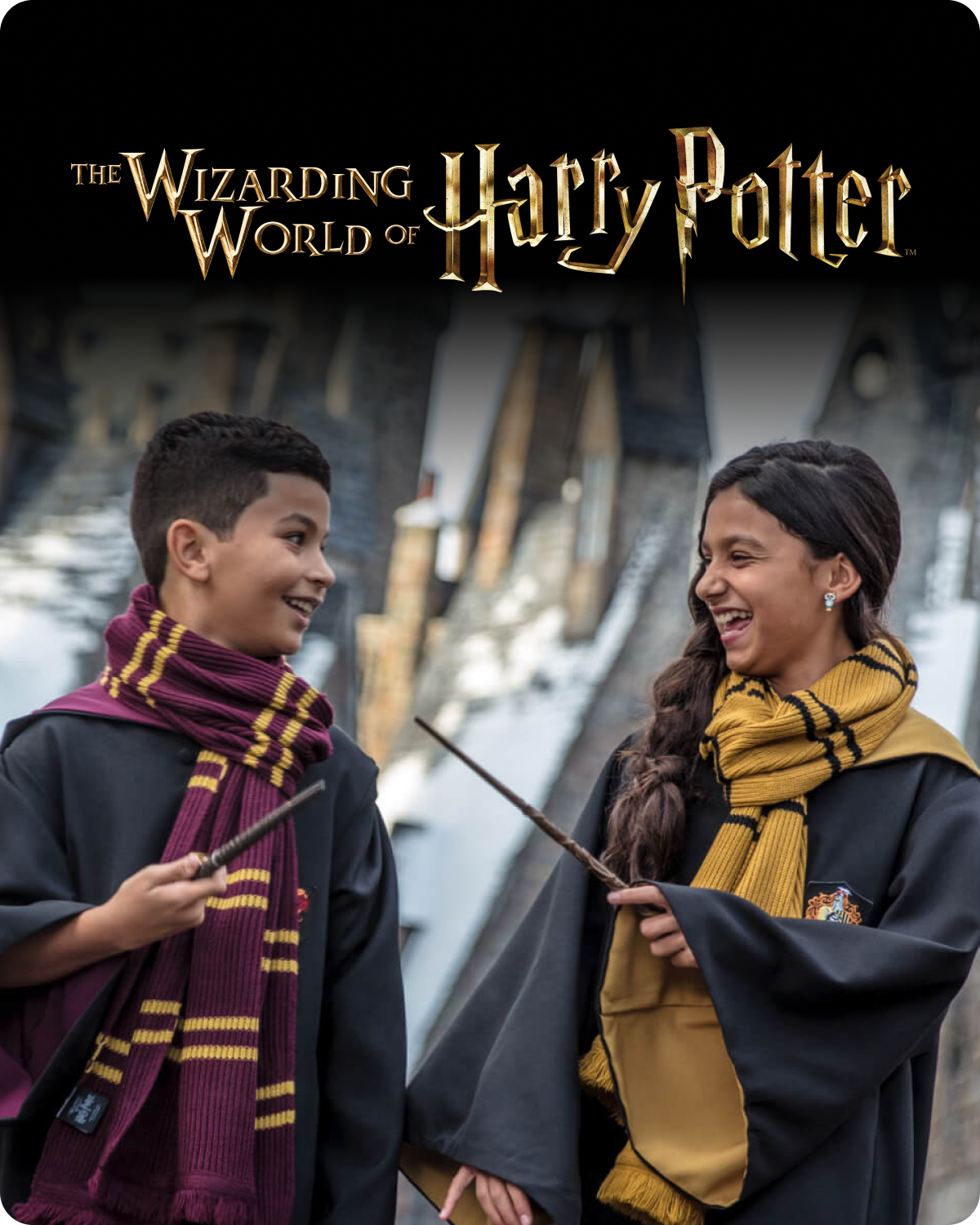 Two people in Harry Potter-themed clothing with wands, standing in front of a castle-like structure - click to shop the Wizarding World of Harry Potter merch now!