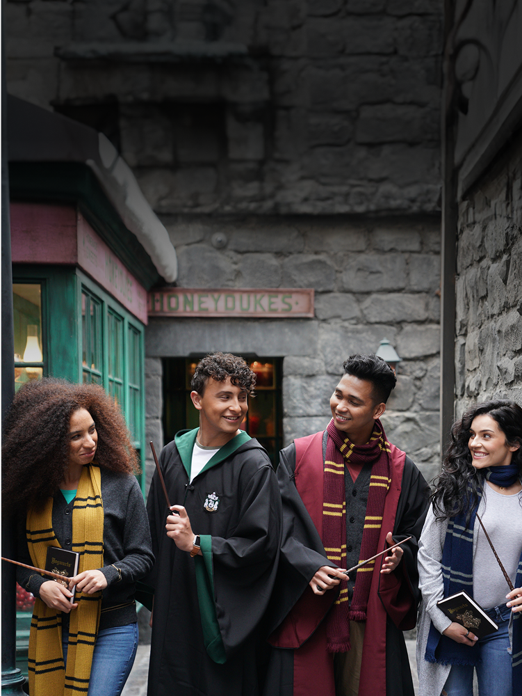 Image showcasing four people in wizard robes and Wizarding World of Harry Potter™ clothing standing in a row, with wands - click to shop Wizarding World of Harry Potter™ Merch now!